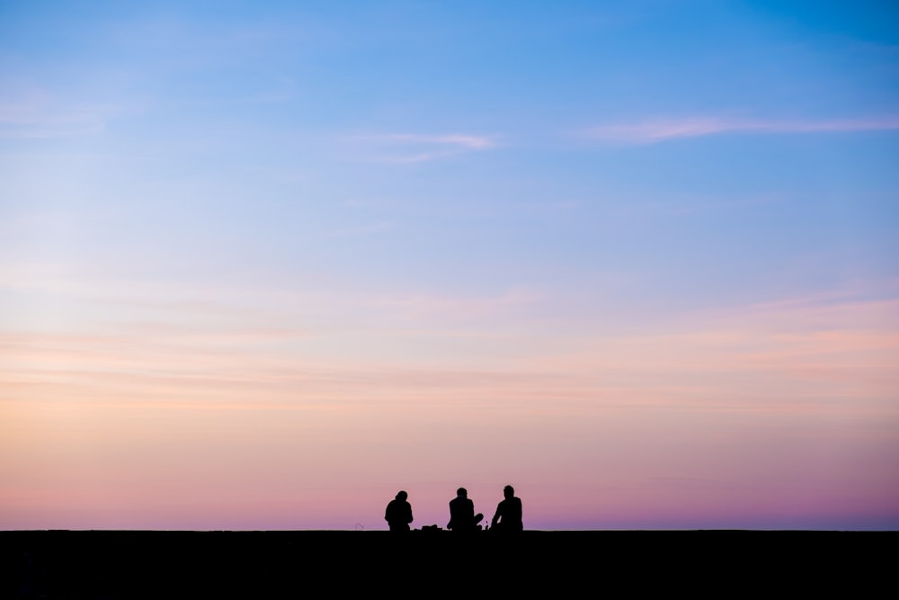 하늘 아래 앉아있는 세 사람의 실루엣 사진