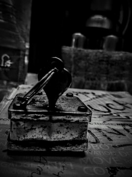 A vintage rubber stamp with a wooden handle sits on a surface covered with printed text. The image is in black and white, giving it a nostalgic, timeless feel. The background is blurred, drawing attention to the stamp's worn details and textures.