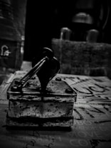 A vintage rubber stamp with a wooden handle sits on a surface covered with printed text. The image is in black and white, giving it a nostalgic, timeless feel. The background is blurred, drawing attention to the stamp's worn details and textures.