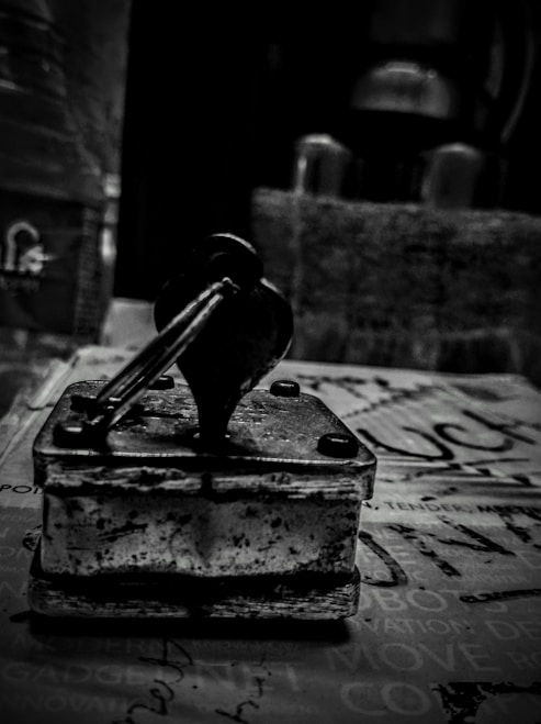 A vintage rubber stamp with a wooden handle sits on a surface covered with printed text. The image is in black and white, giving it a nostalgic, timeless feel. The background is blurred, drawing attention to the stamp's worn details and textures.