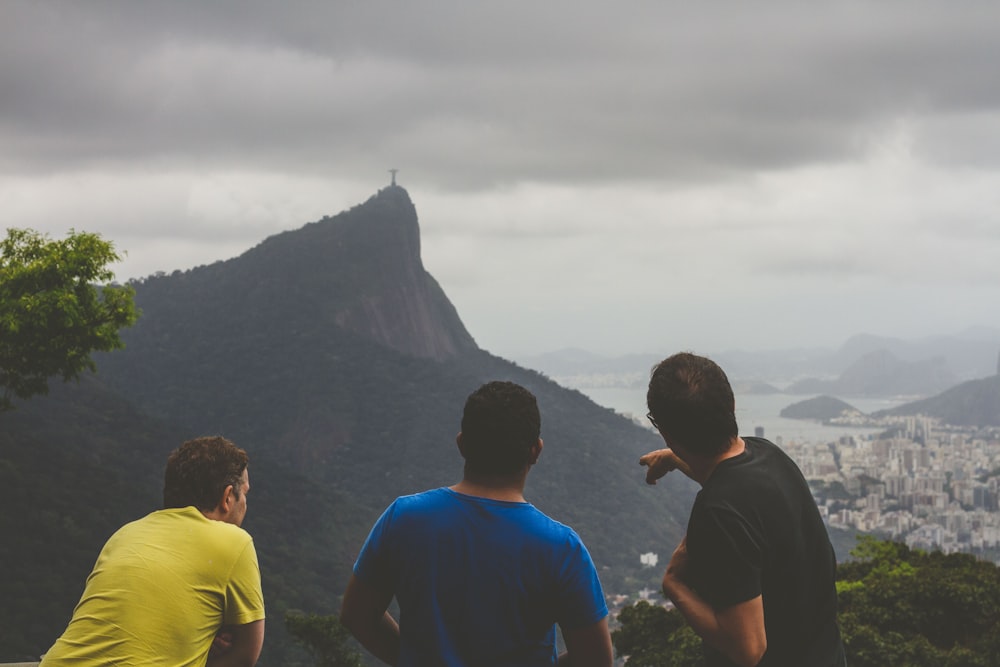 a group of three men sitting on top of a lush green hillside