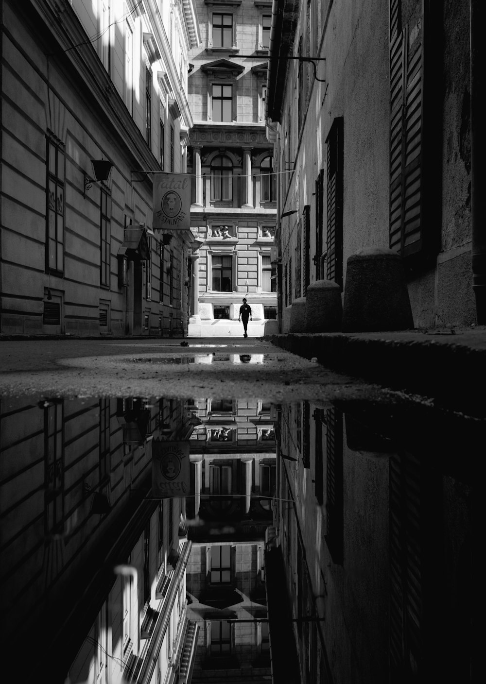 grayscale photo of man about to enter the pathway in between of buildings