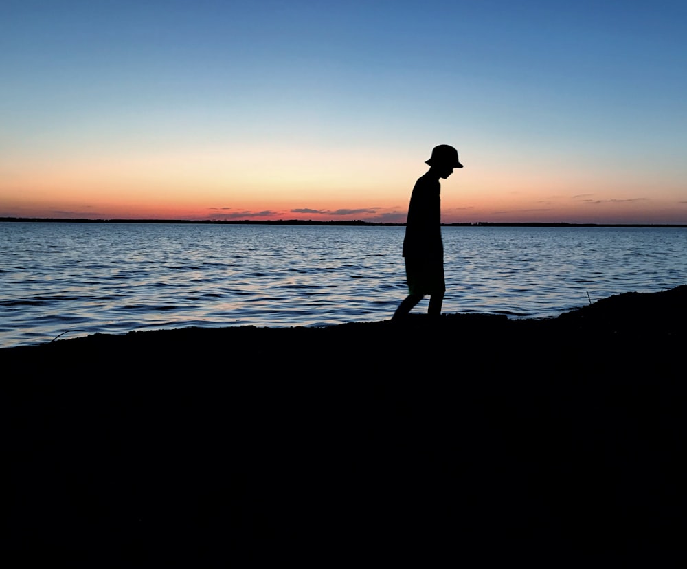 silhouette di persona che cammina vicino allo specchio d'acqua