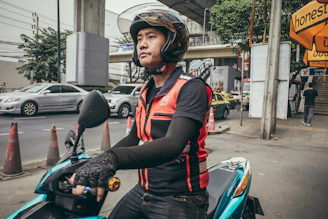 A comfortable motorcycle taxi rider wearing a helmet, ready to pick up a passenger in an urban setting.