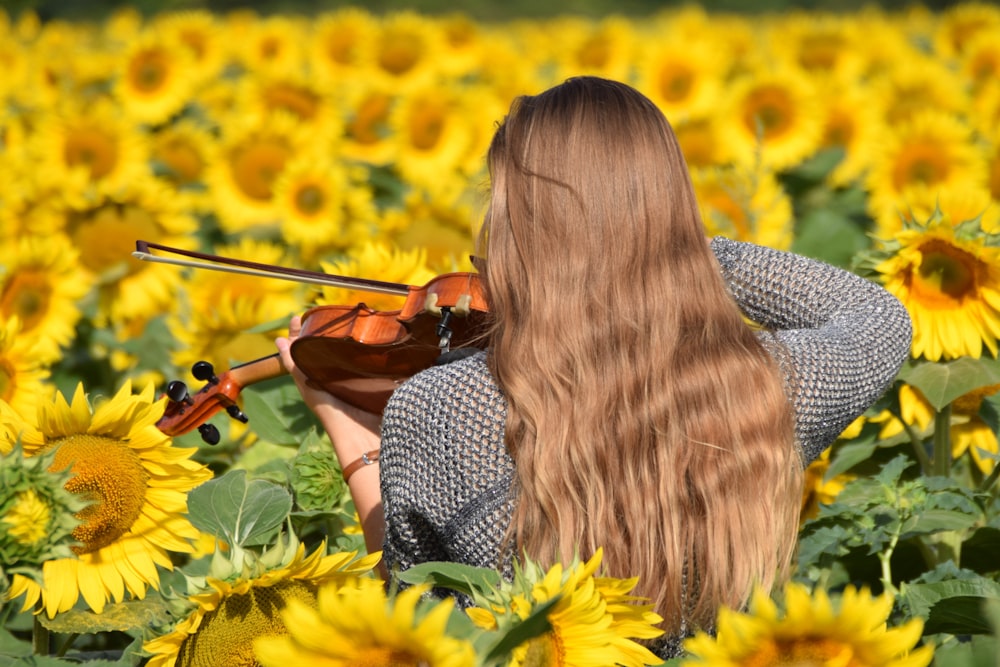 woman playing brown violin surrounded by bed of sunflowers