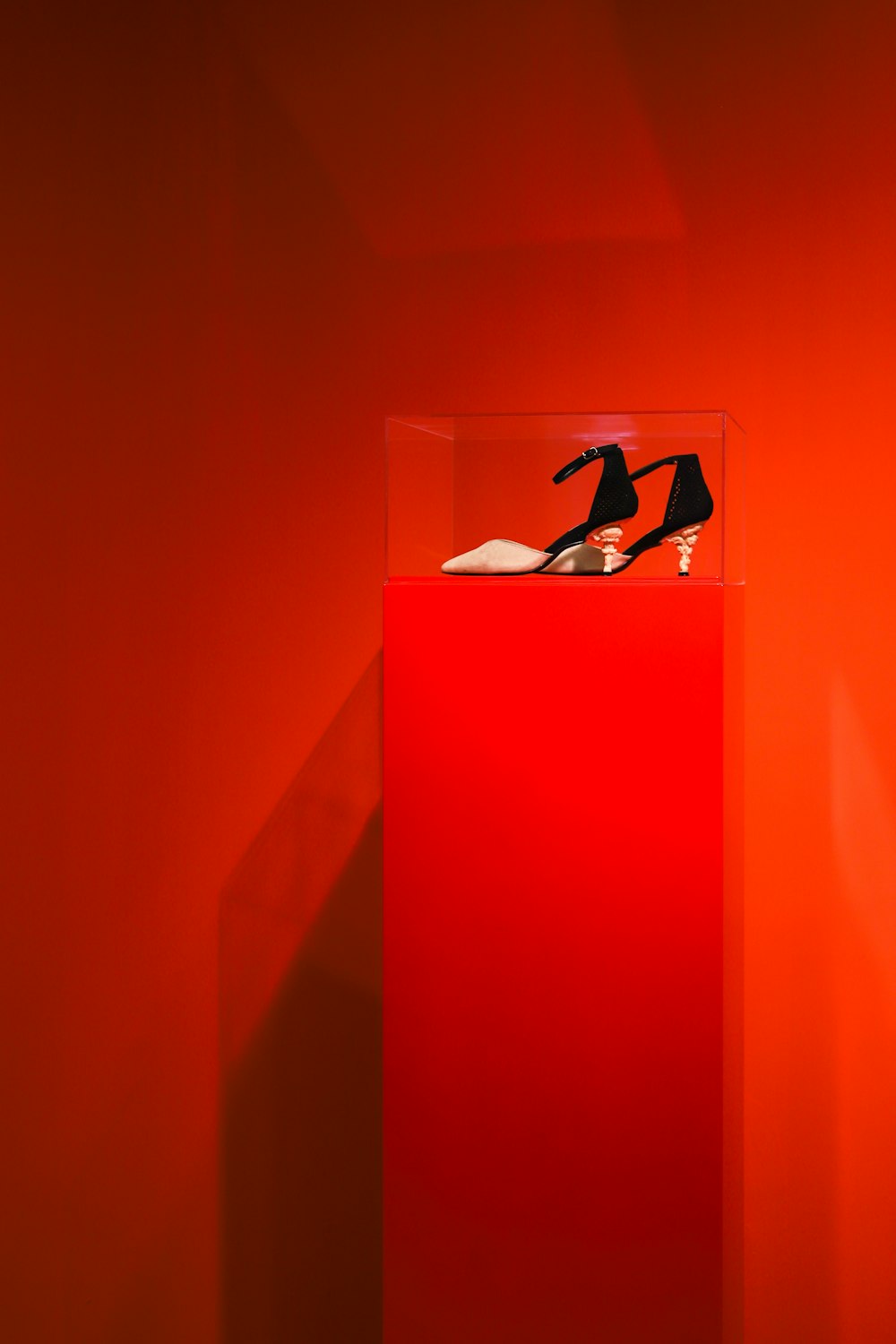 black-and-brown ankle-strap heeled sandals on red and clear glass display counter