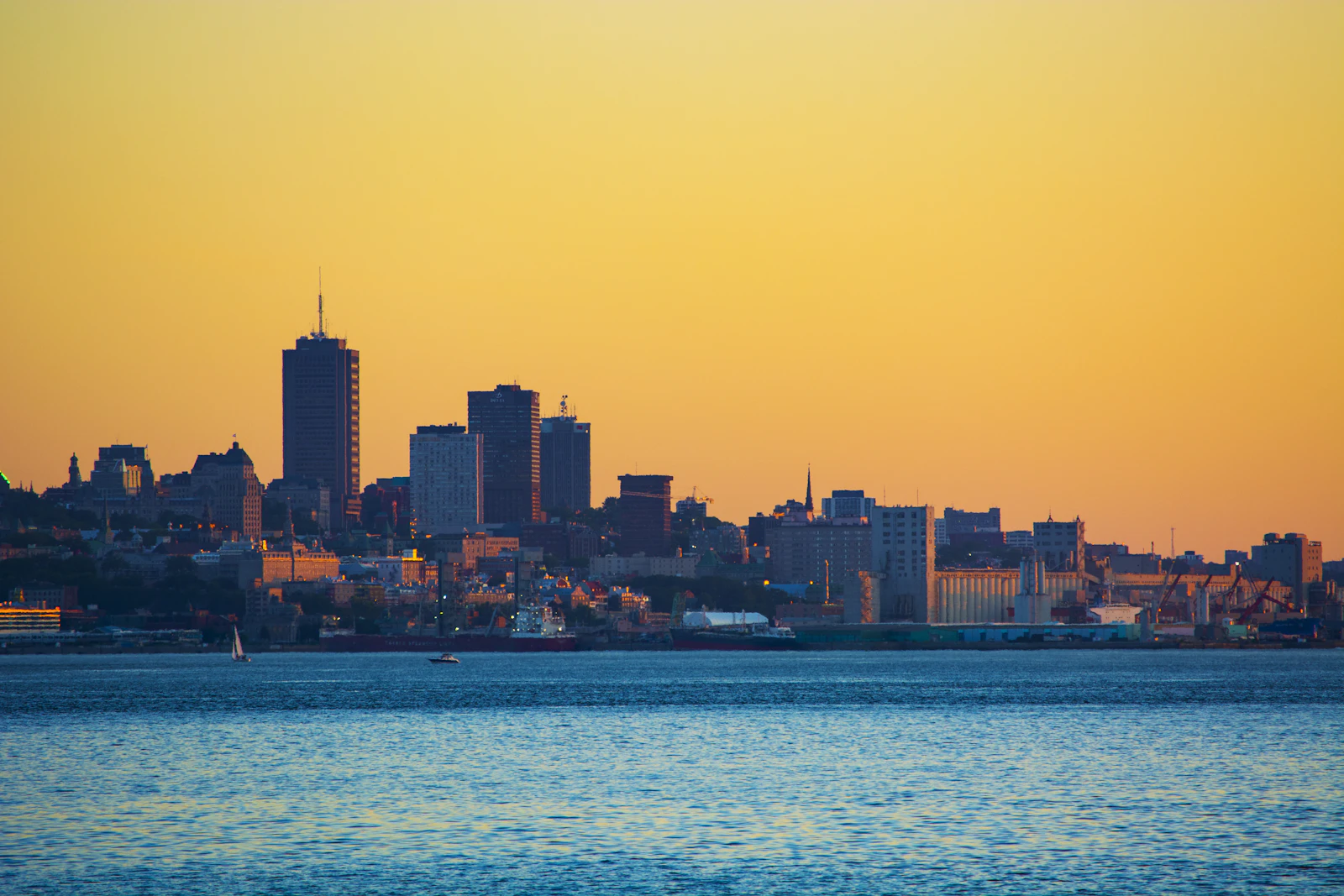 Quebec City buildings glowing at sunset above the water with boats in the foreground
