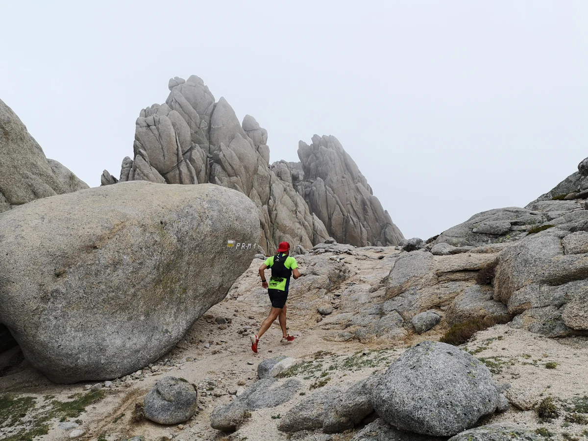 Corredor de trail abriéndose paso entre formaciones rocosas de granito, en terreno técnico y exigente