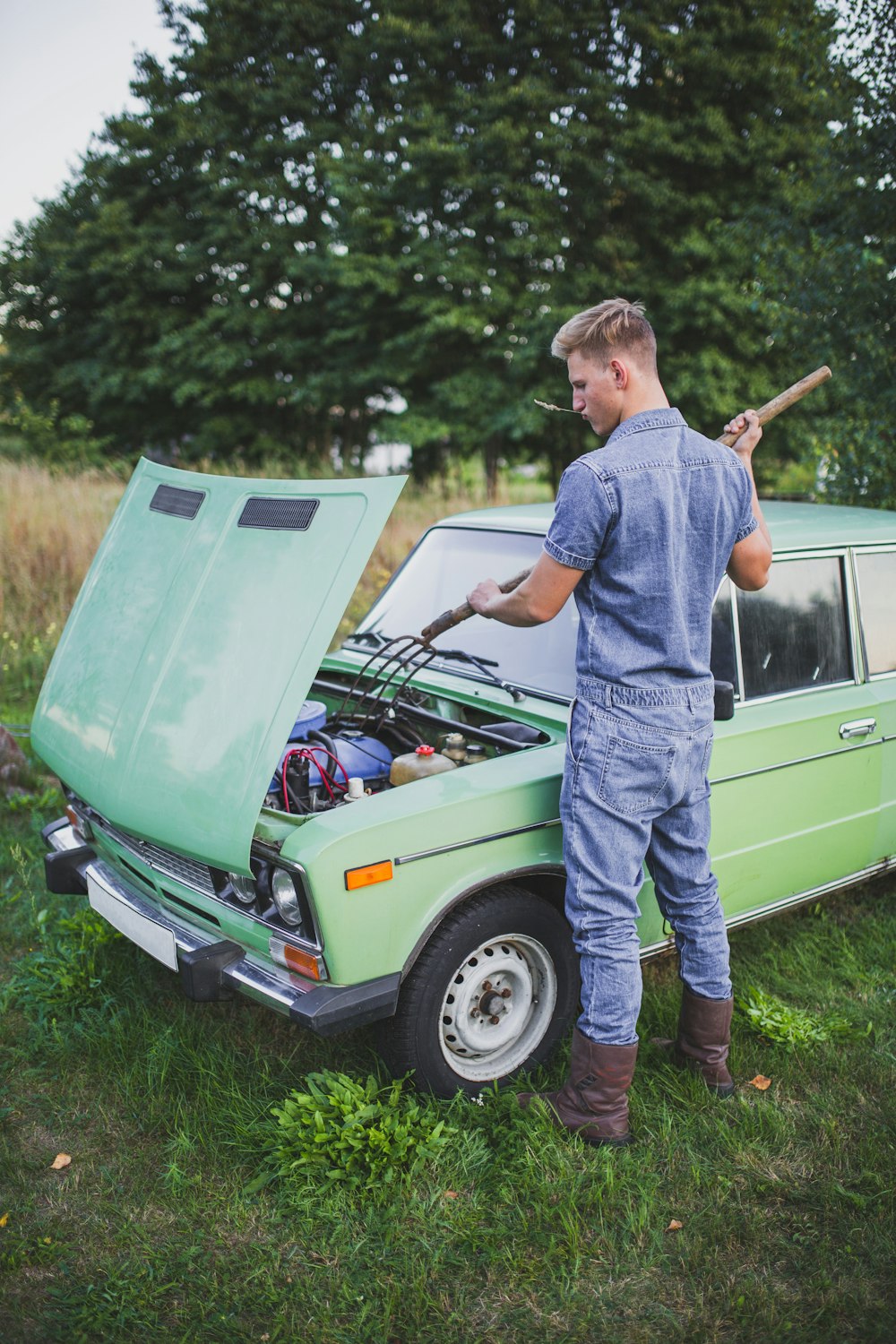 man in blue top fixing green car during daytime