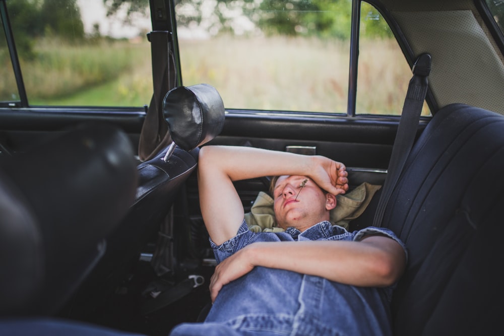 person in blue denim shirt sleeping behind the car seat