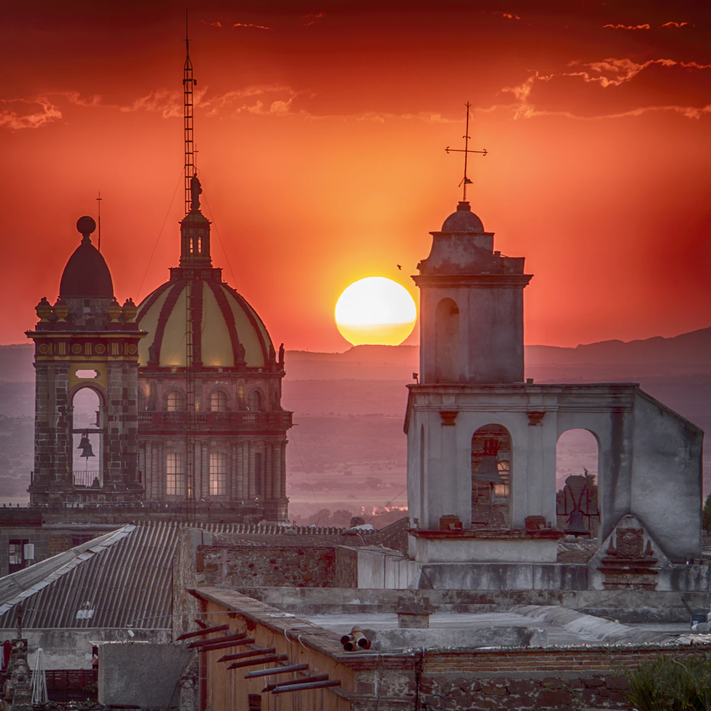 San Miguel de Allende sunset with the dramatic red and orange sky behind the gold church dome and bell towers of La Parroquia
