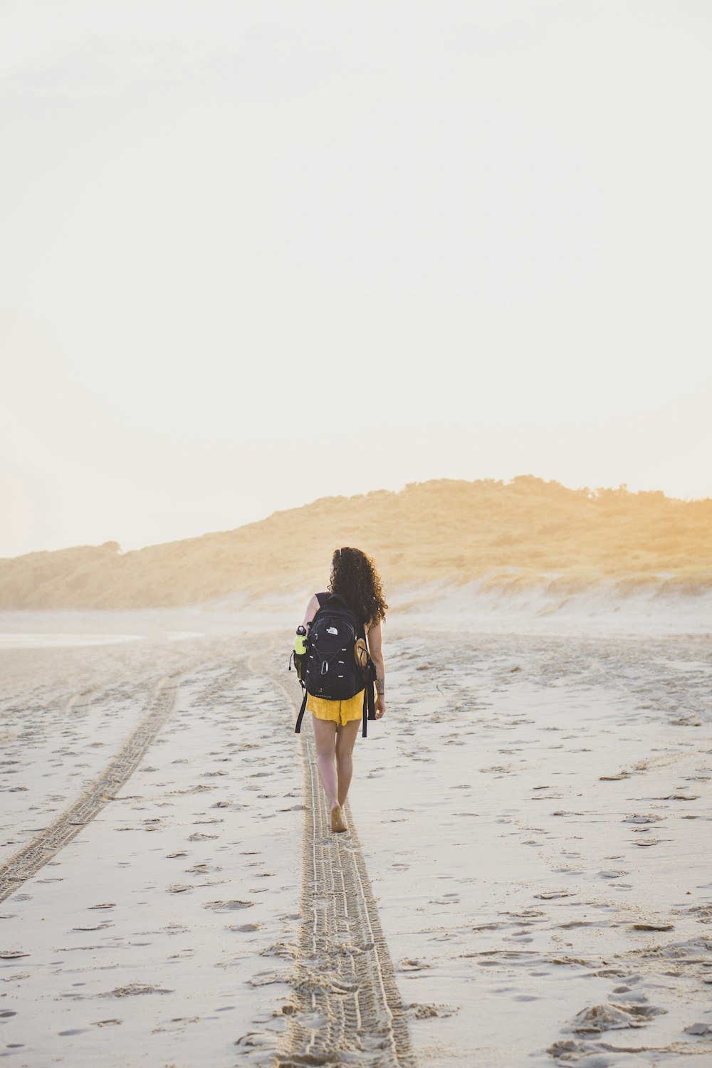 woman wearing yellow bottoms walking on sand during daytime