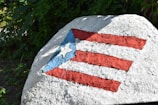 A large rock painted with the flag of Puerto Rico, featuring red and white stripes and a blue triangle with a white star.