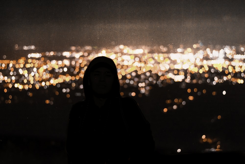 Homem vestindo capuz pullover preto com vista para as luzes da cidade durante a noite