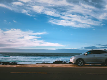 A shiny white SUV cruising along a coastal highway with ocean waves in the background.