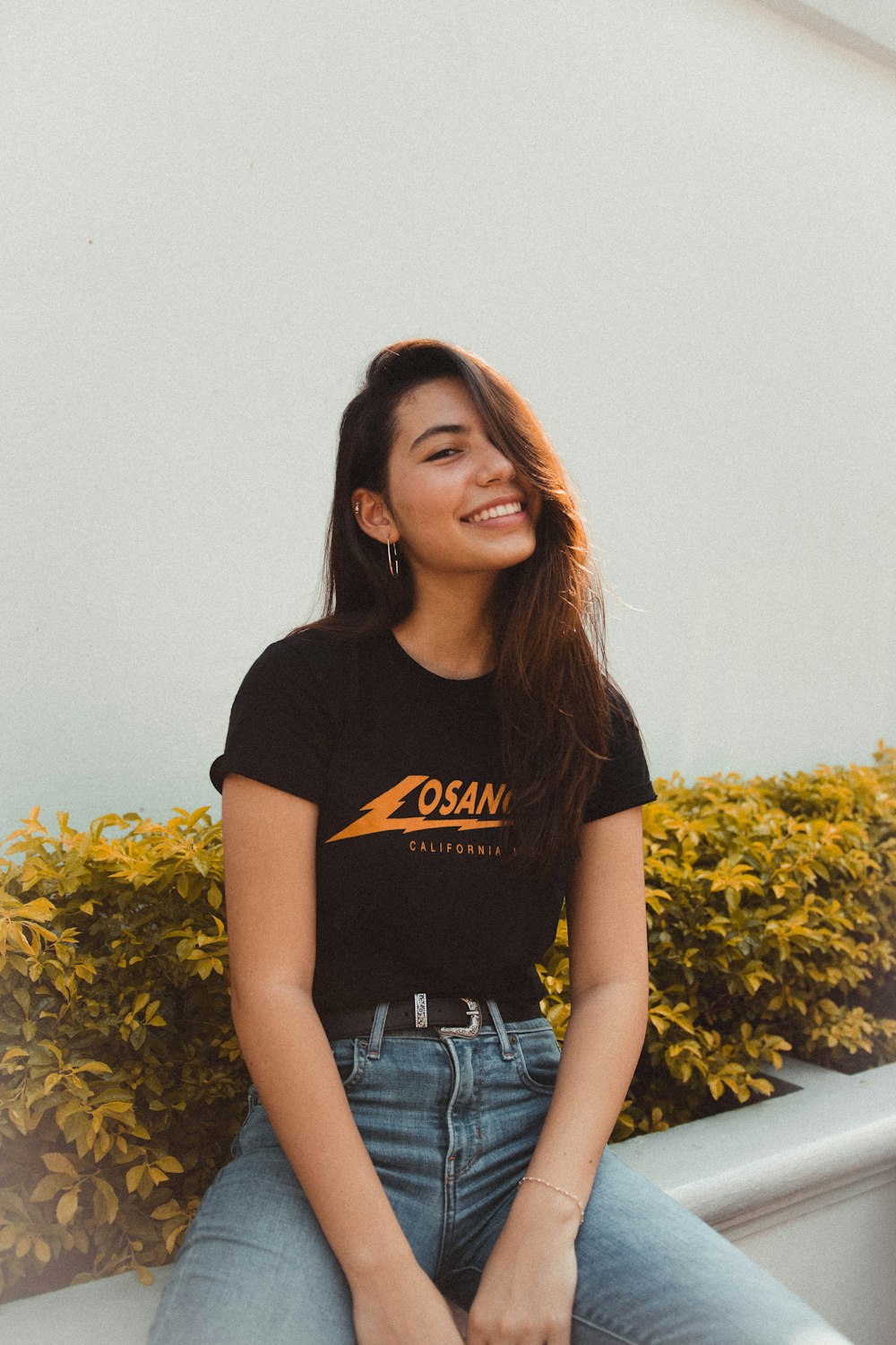 Mujer sonriente con camisa negra y naranja y pantalones de mezclilla azul