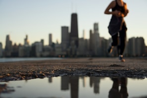 A dynamic shot of a man jogging in Lumina Apparel activewear along a riverside path with city skyline in the background.