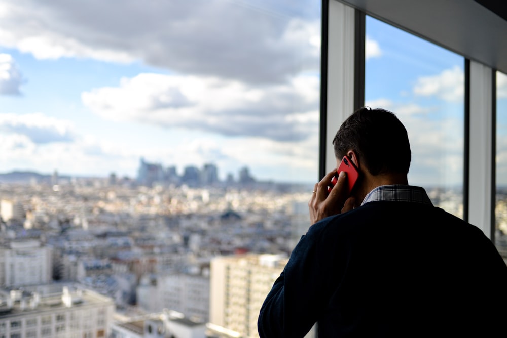 man in black top using red phone by glass wall