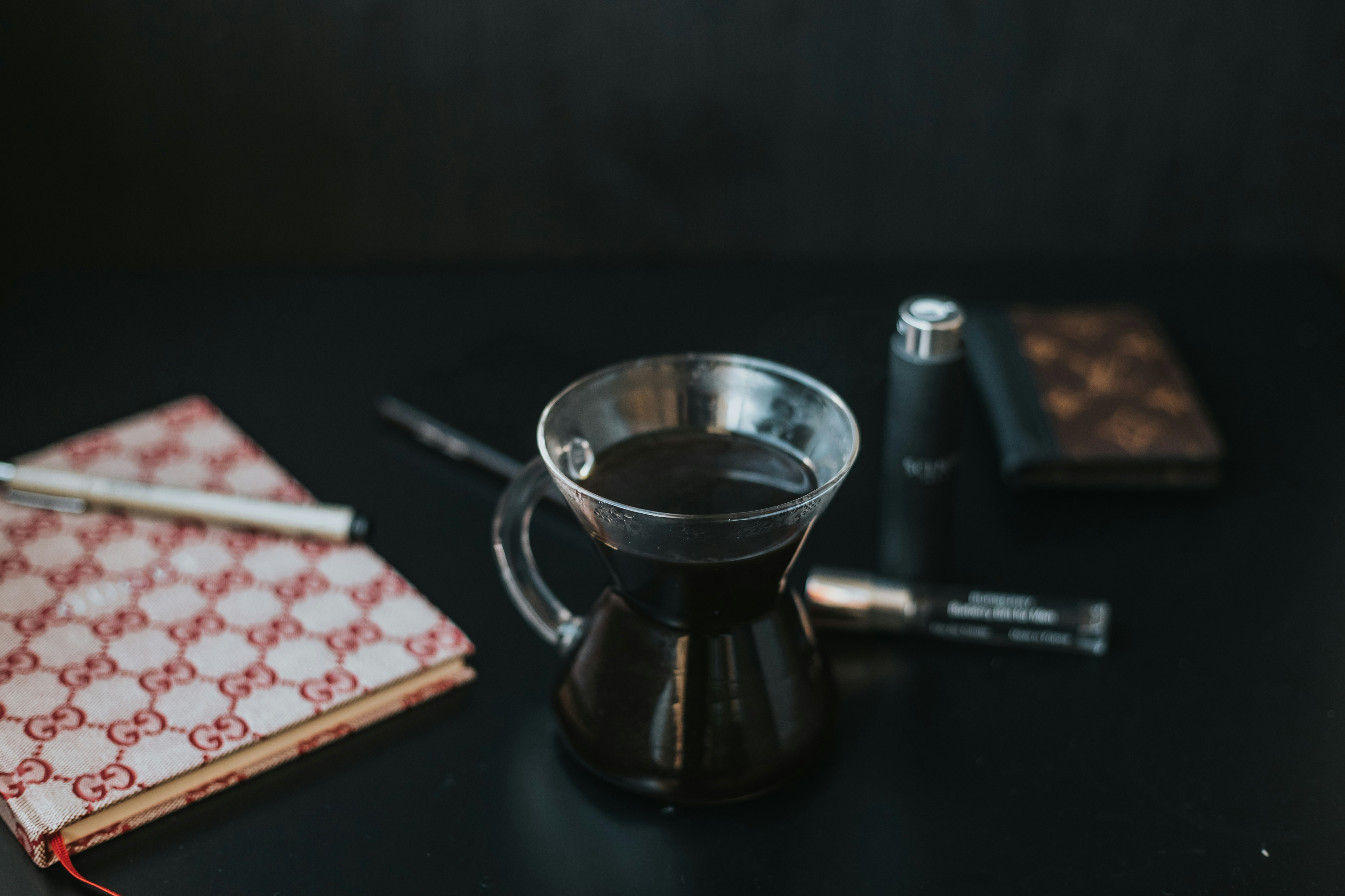 Glass mug of black coffee beside a notebook