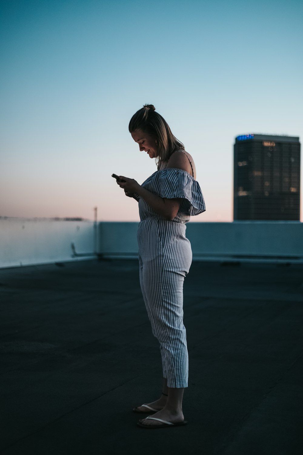 woman standing on rooftop smiling white using smartphone