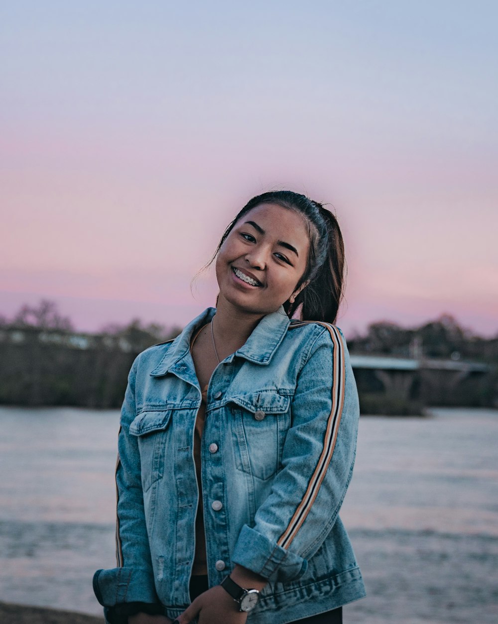 smiling woman in blue denim jacket by body of water