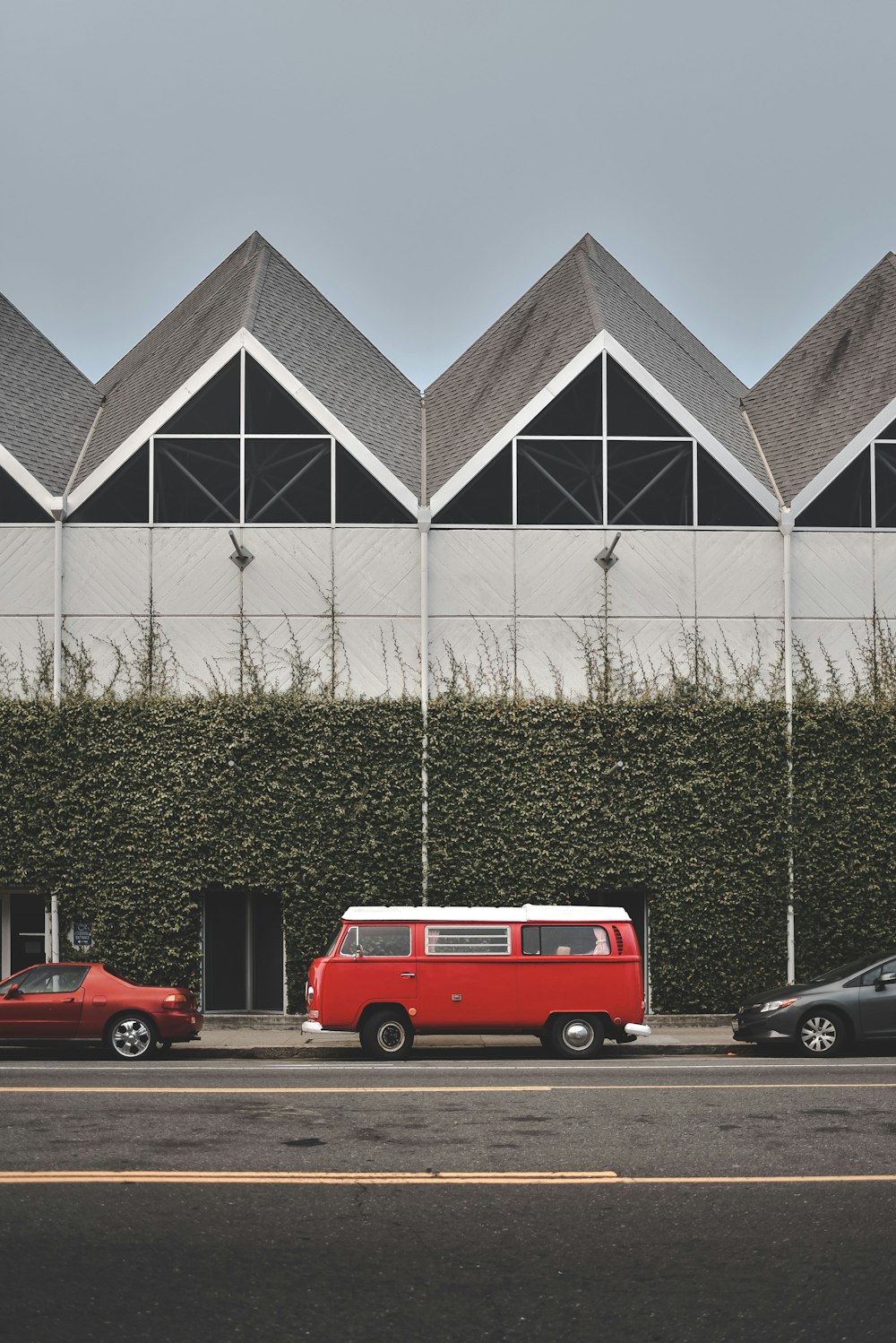 赤と白のフォルクスワーゲンのバンは、つるで覆われた壁の前に駐車