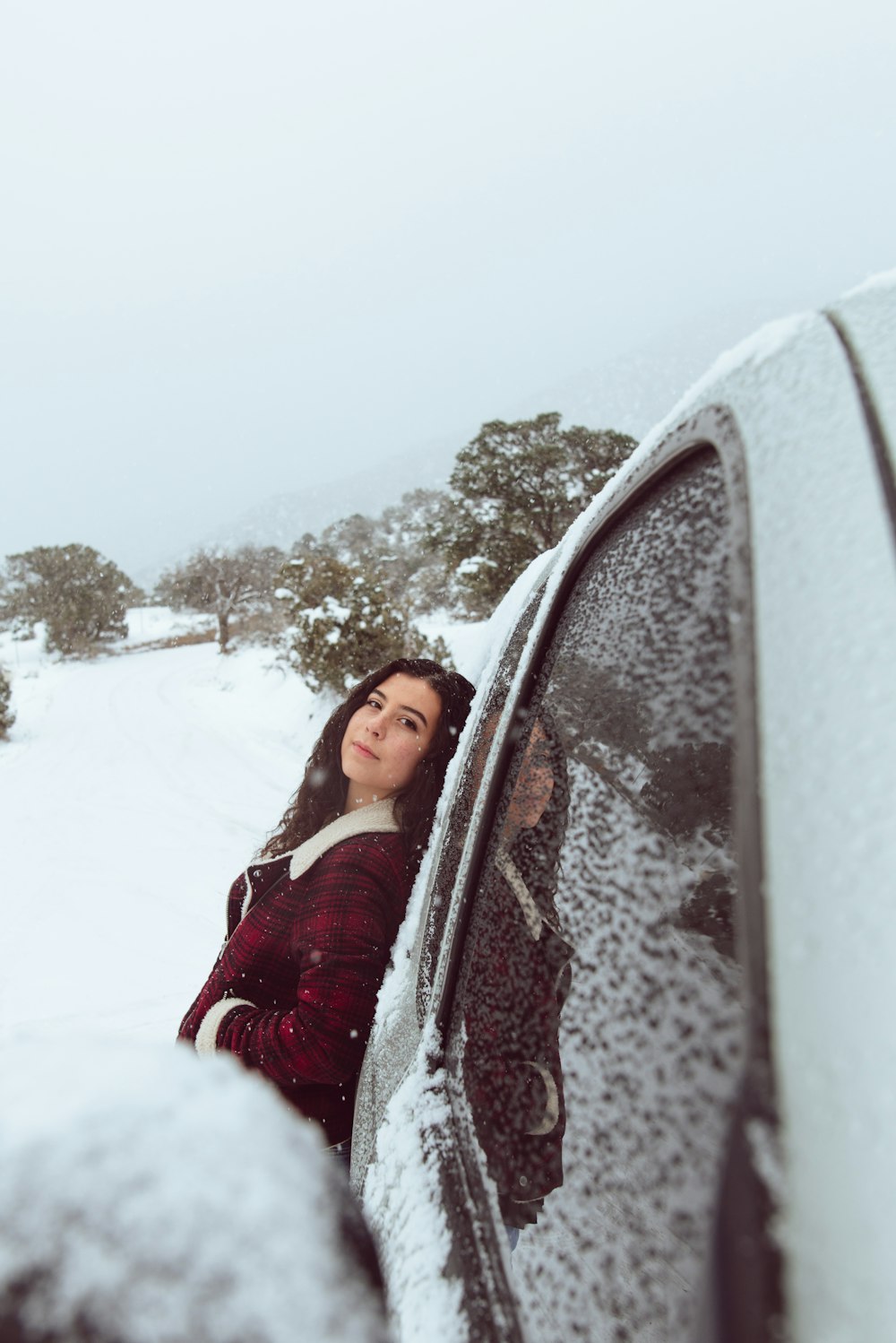 Donna in giacca rossa e bianca che si appoggia all'automobile durante la stagione invernale