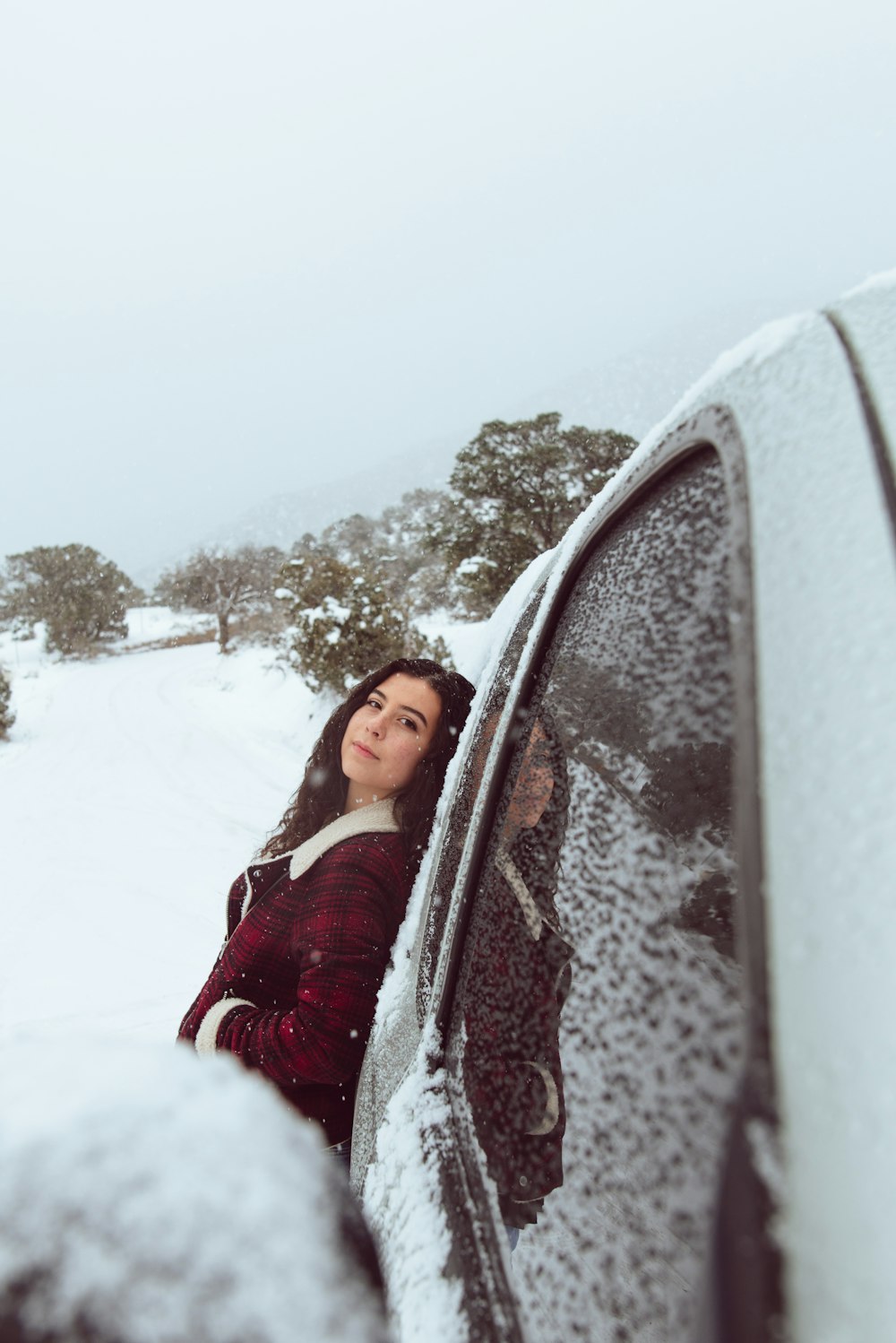 woman in red and white jacket leaning on car during winter season