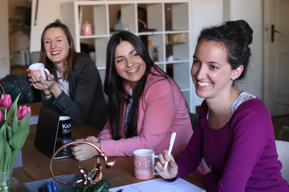 three women sitting by the table having coffee and smiling