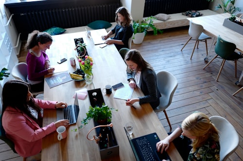 Aerial view of five employees working at a wood table in an office space.