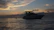 A serene luxury yacht anchored in a calm Urla bay at sunset, with soft golden light reflecting on the water.