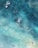 Bird's-eye view of people surfing or paddling in the ocean. The water appears clear with varying shades of blue and turquoise, and sunlight reflects off the surface. There are three individuals visible, each on a surfboard, separated by the vast, shimmering water.
