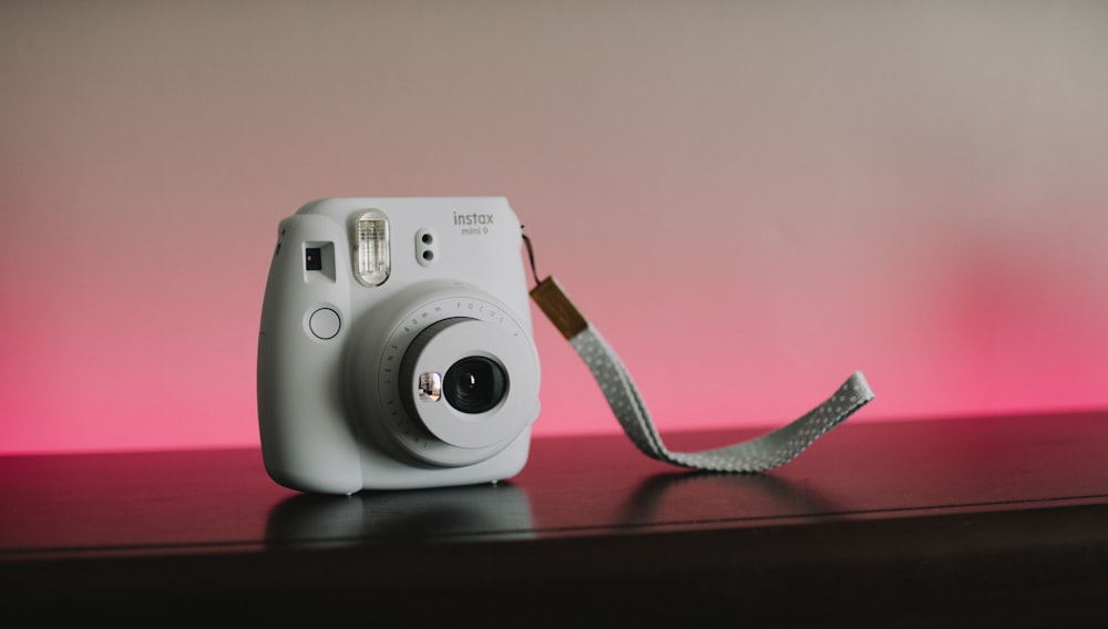 Cámara Fujifilm Instax blanca sobre superficie de madera marrón