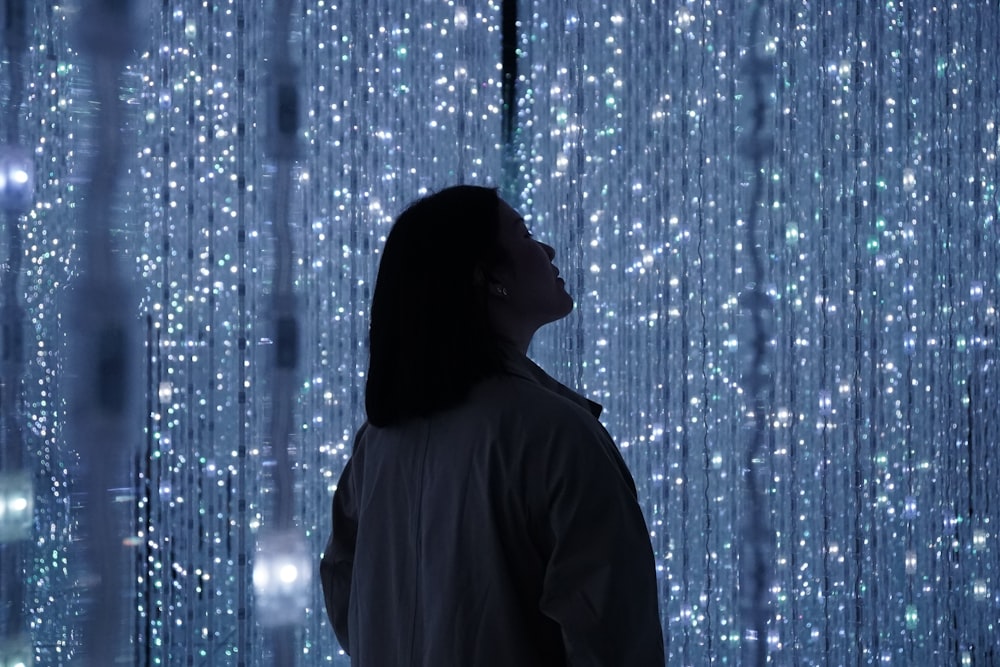 silhouette of woman looking up beside string lights