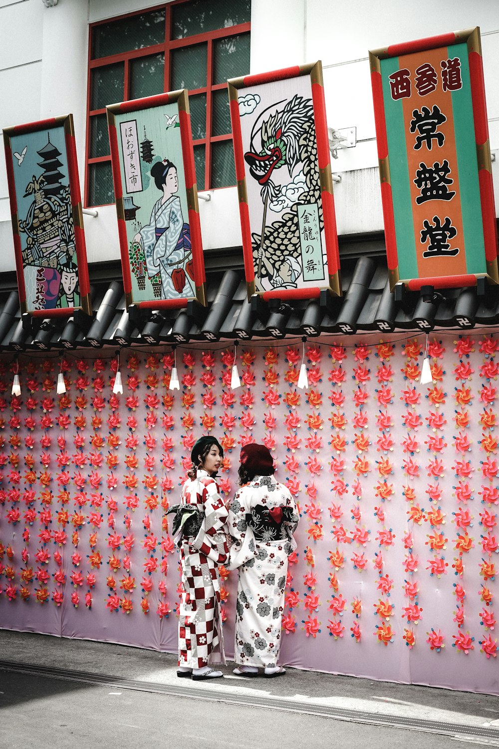 two women wearing white-and-black traditional dresses standing beside wall