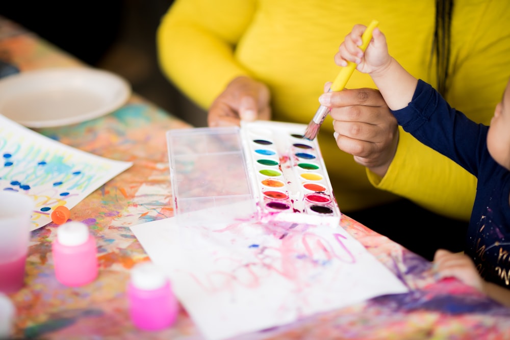 toddler holding paintbrush standing beside woman holding water paint