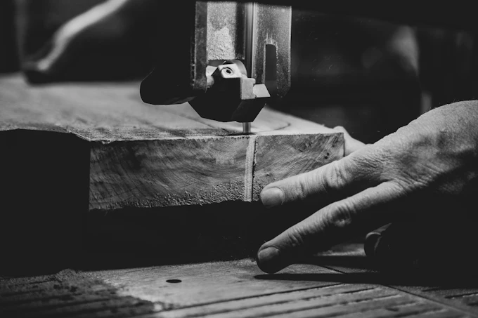 A hand steadying a board at the shop machine