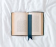 an open book with a blue ribbon on a white sheet