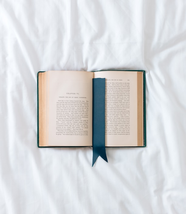 an open book with a blue ribbon on a white sheet