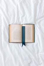 an open book with a blue ribbon on a white sheet