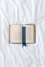 an open book with a blue ribbon on a white sheet