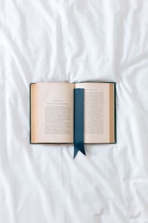 an open book with a blue ribbon on a white sheet