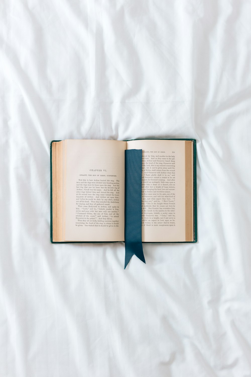 Un libro abierto con una cinta azul sobre una sábana blanca