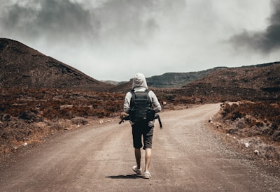 man in gray hoodie carrying backpack walking under the sun