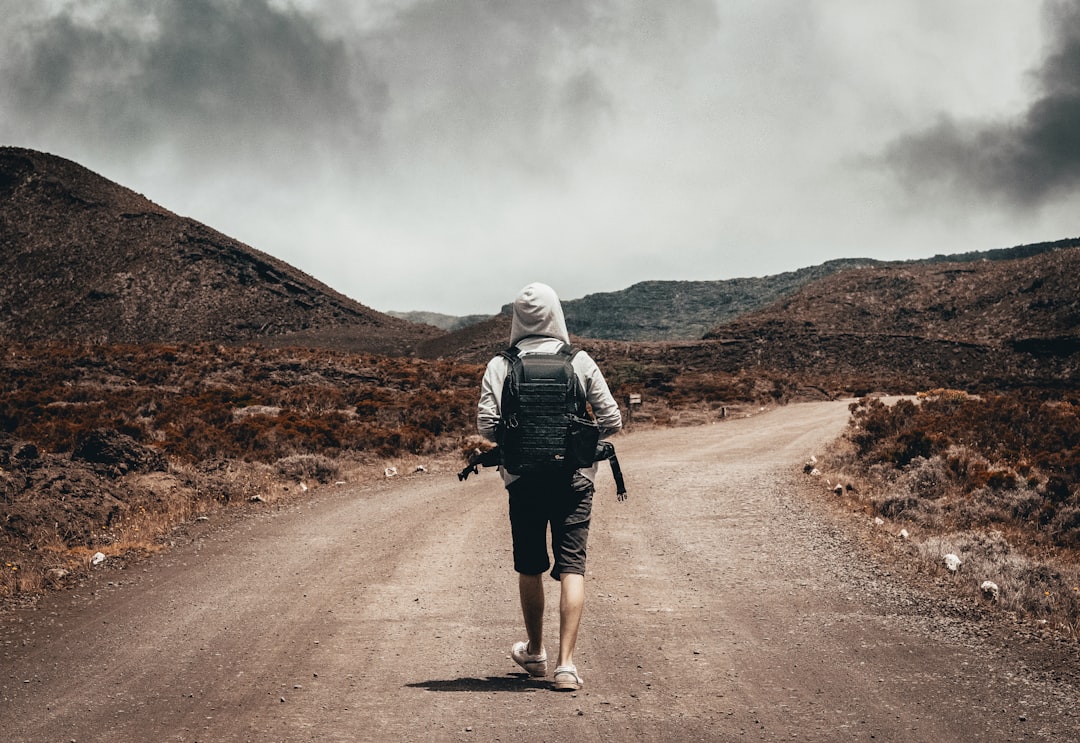 man in gray hoodie carrying backpack walking under the sun,
