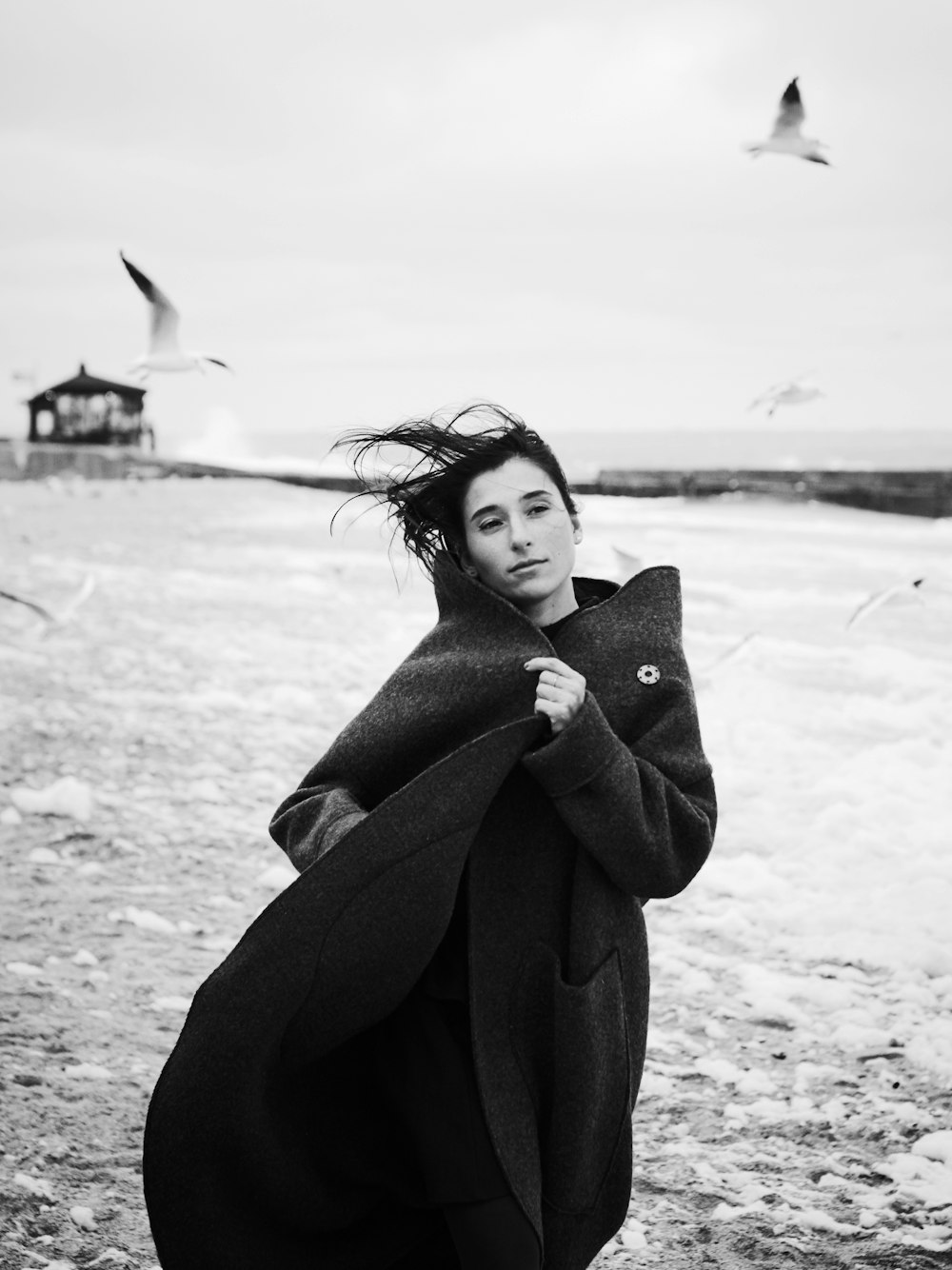 mulher no casaco preto andando com as gaivotas voando
