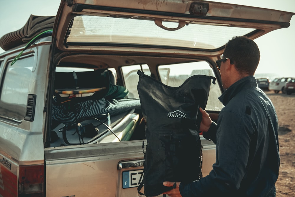 man loading black bag in back of suv