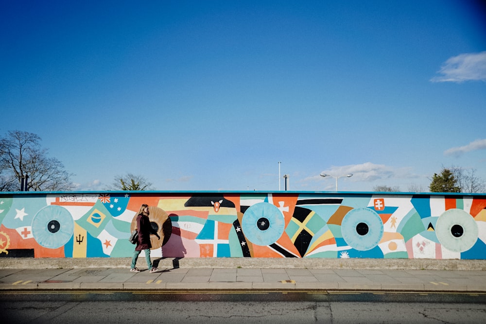 woman walking along sidewalk with mural paintings on wall