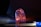 A translucent, irregularly shaped crystal or glass object sits on a reflective surface. It is illuminated by colorful lighting, primarily in shades of blue, orange, and pink, creating a glowing effect. The background is dark, enhancing the vibrant colors and the object's clarity.