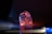 A translucent, irregularly shaped crystal or glass object sits on a reflective surface. It is illuminated by colorful lighting, primarily in shades of blue, orange, and pink, creating a glowing effect. The background is dark, enhancing the vibrant colors and the object's clarity.